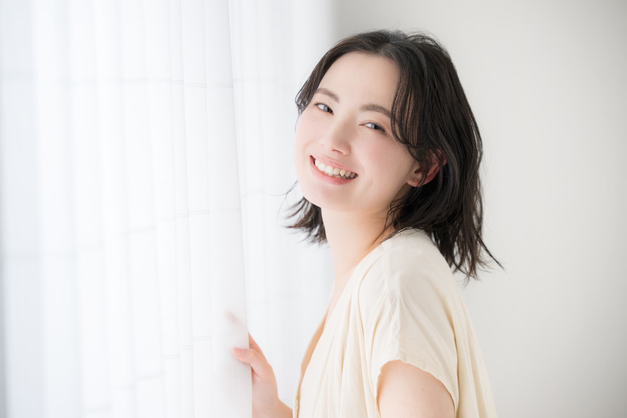 窓際で朝日を浴びてカーテンを開けようとしている笑顔の女性